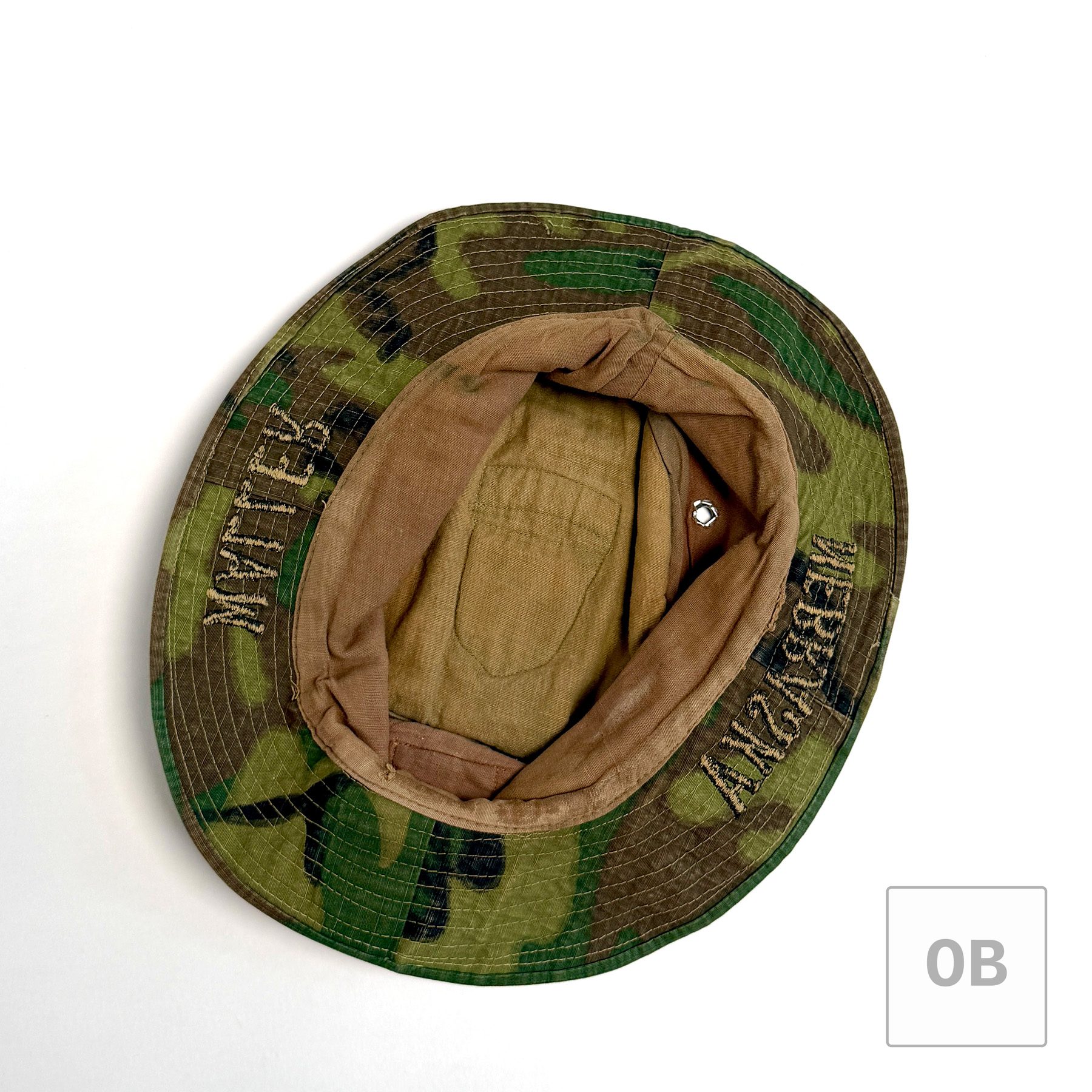 Interior of the ERDL boonie hat showing a tan cotton lining, a ventilation eyelet, and the reverse of the WALLER and NEBRASKA embroidery stitched through the brim.