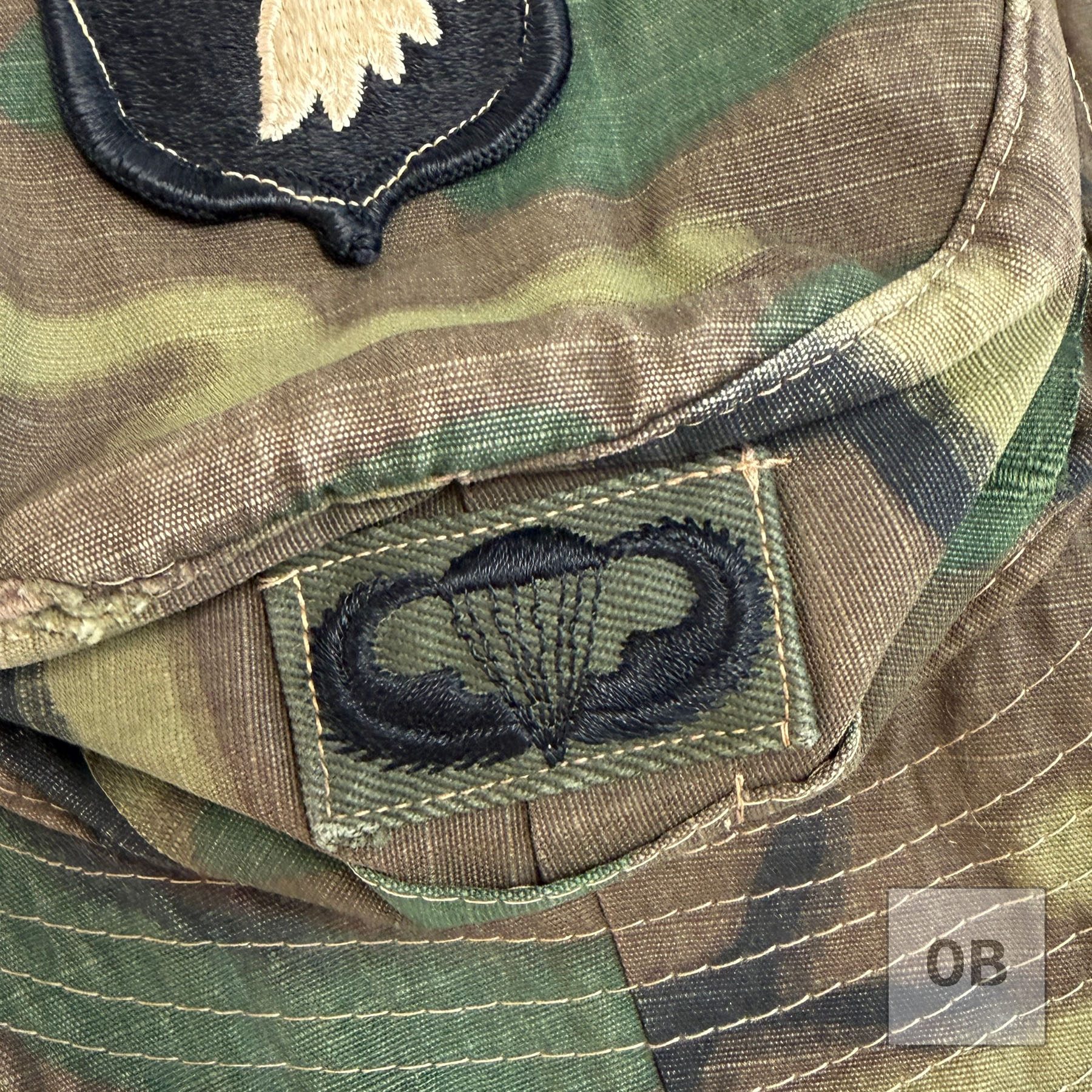 Close-up of theater-made subdued parachutist wings embroidered in black on an olive drab tab, sewn to the crown band of the hat.