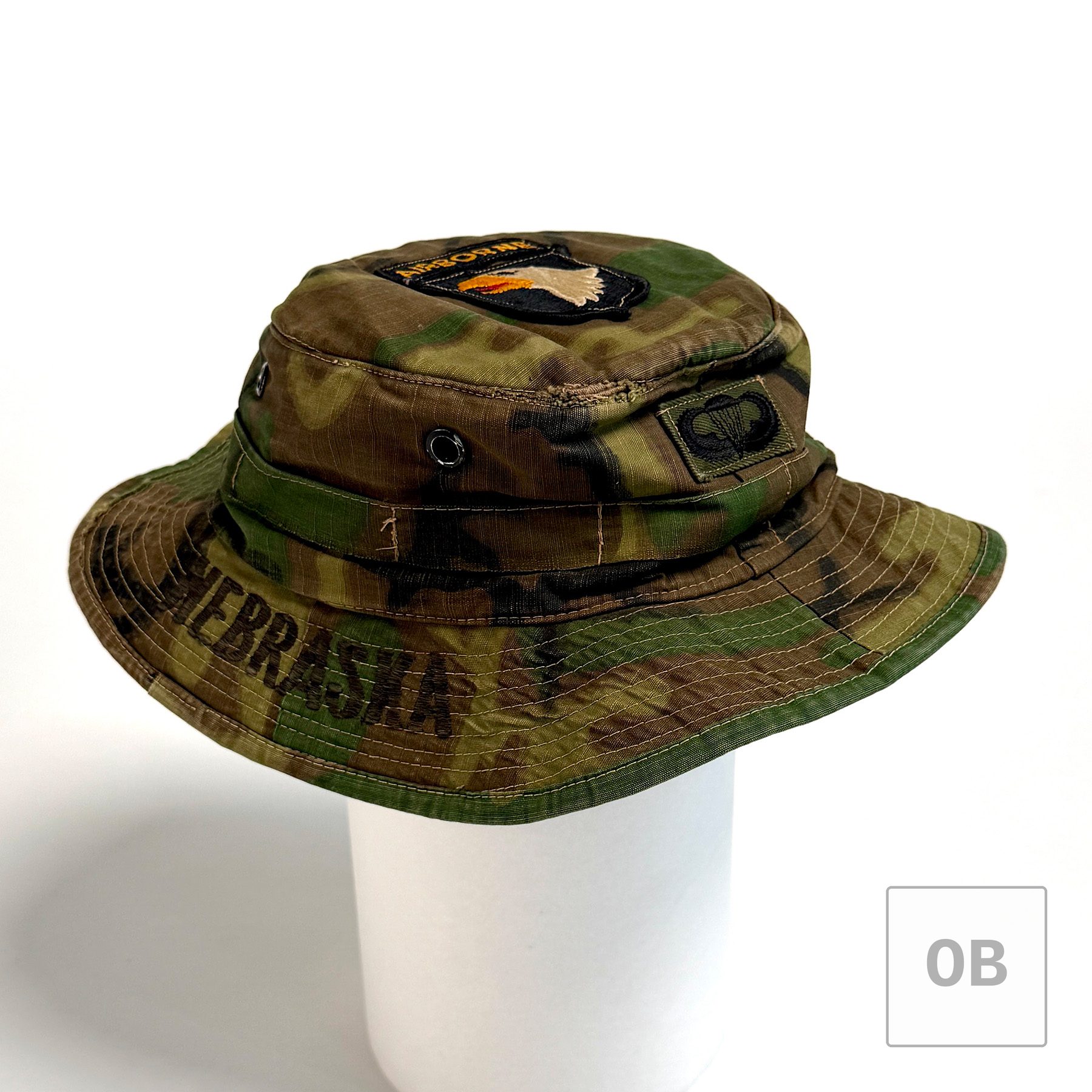 The ERDL boonie hat on a white display form, turned to show NEBRASKA embroidered on the brim and subdued parachutist wings on the crown band.