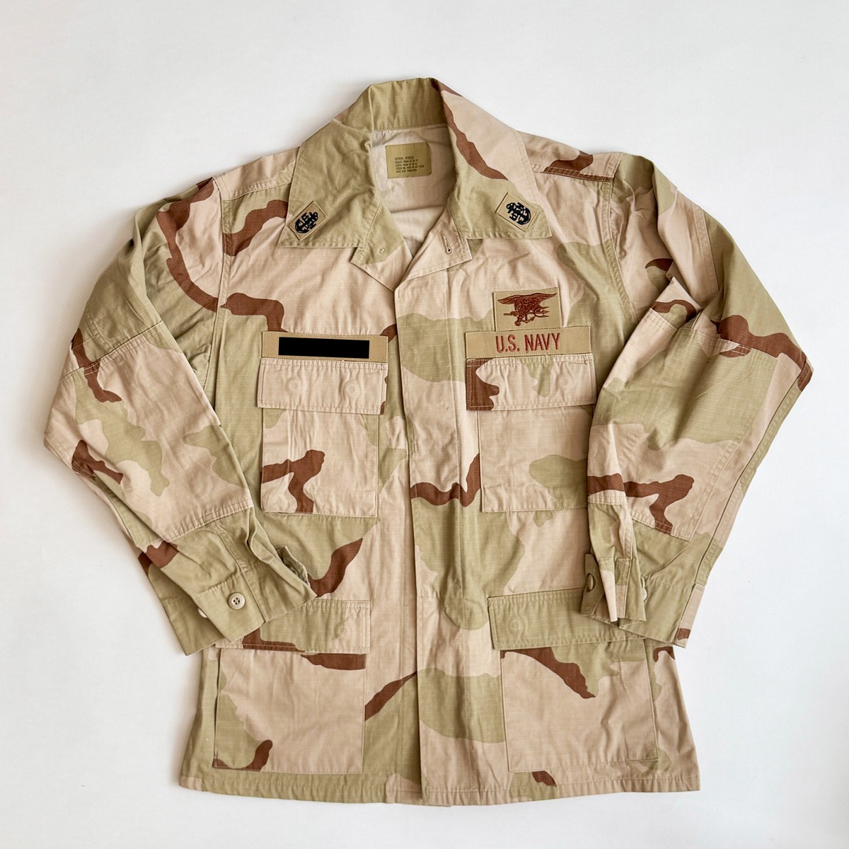 Six-color Desert Camouflage Uniform top laid flat, name tape covered above the left breast pocket.