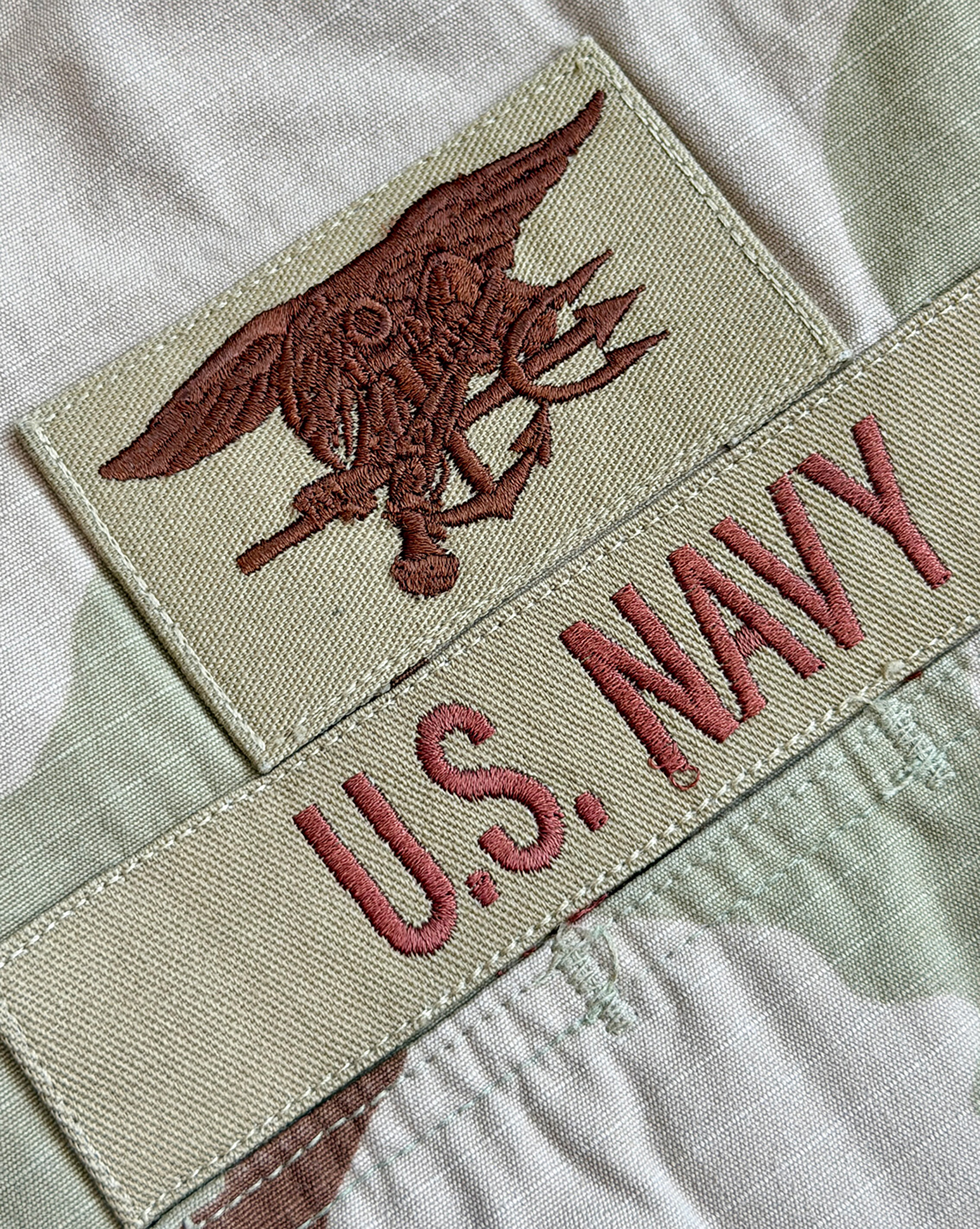 Close-up of the wide, open point collar — the "Elvis collar" cut of early production DCU tops — with a Naval Special Warfare device pin, Trident patch, and U.S. NAVY branch tape.