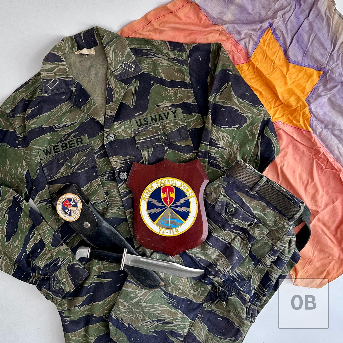 Grouped tigerstripe camouflage uniform, Buck knife, Task Force 116 plaque, and Viet Cong flag associated with a PBR riverine veteran.