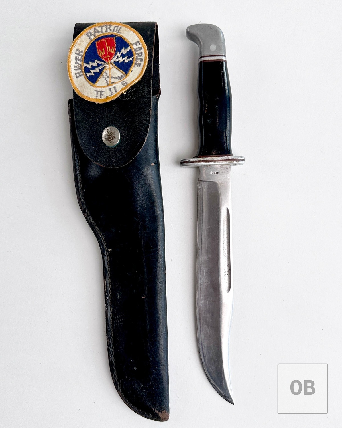 Buck knife beside its sheath, fitted with a River Patrol Force patch.