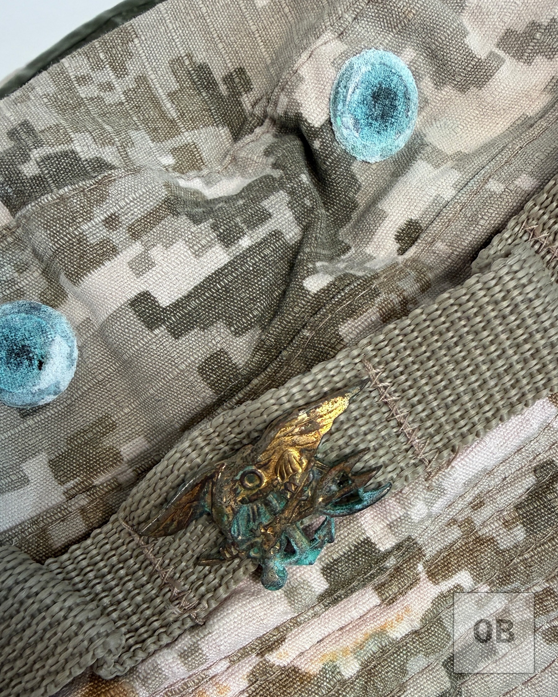 Small, heavily corroded gold-toned Navy SEAL Trident insignia pin, known informally as the Budweiser, affixed to the hat's tan nylon foliage band.
