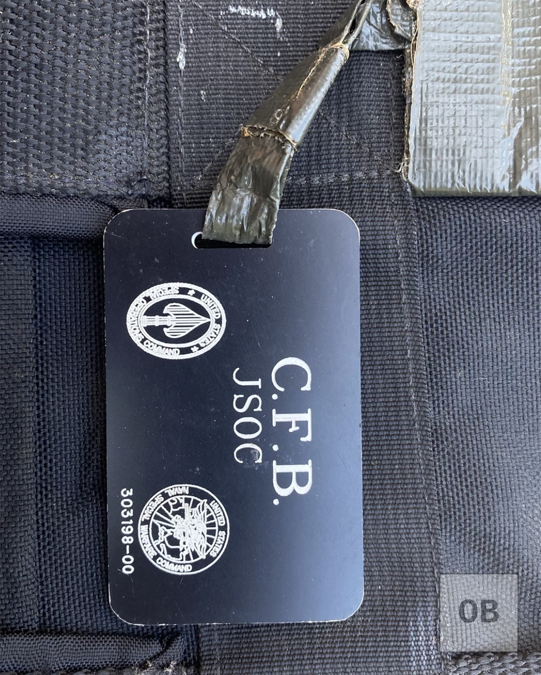 Plastic luggage tag reading C.F.B. and JSOC, printed with the Joint Special Operations Command and Naval Special Warfare Command emblems and a unique identification number, from a Blackhawk bag sold separately before it could be acquired.