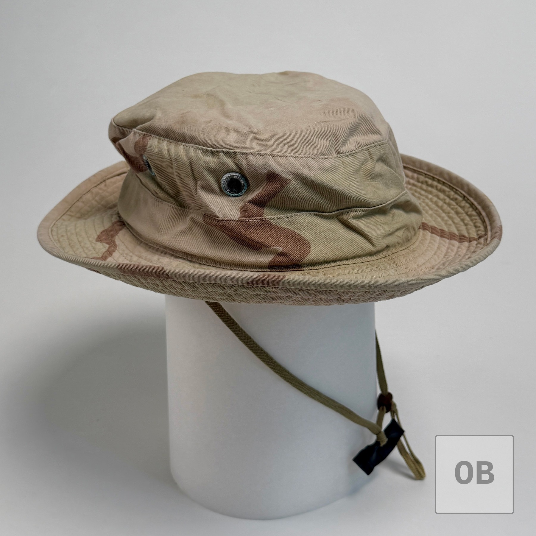 Side view of a three-color desert camouflage boonie hat on a display form, faded from wear.