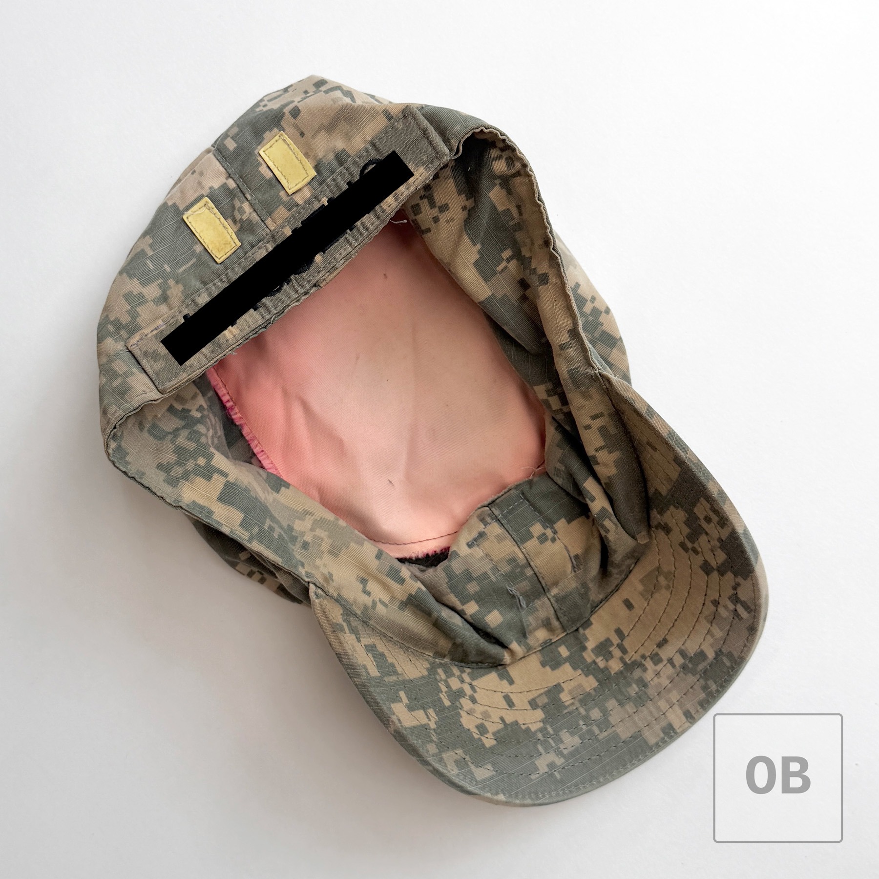 Interior of the UCP patrol cap, showing NCO rank tabs, redacted name tape, and a cut-down panel marker sewn in as a pocket.