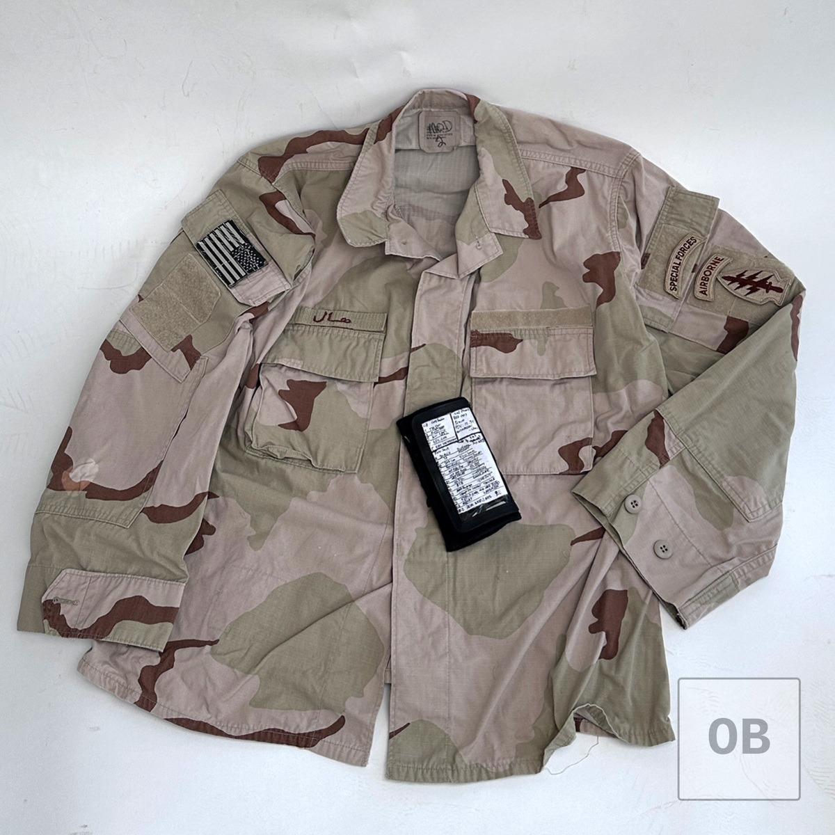 Modified Special Forces DCU top with wrist coach, name tape, and unit patches laid flat.