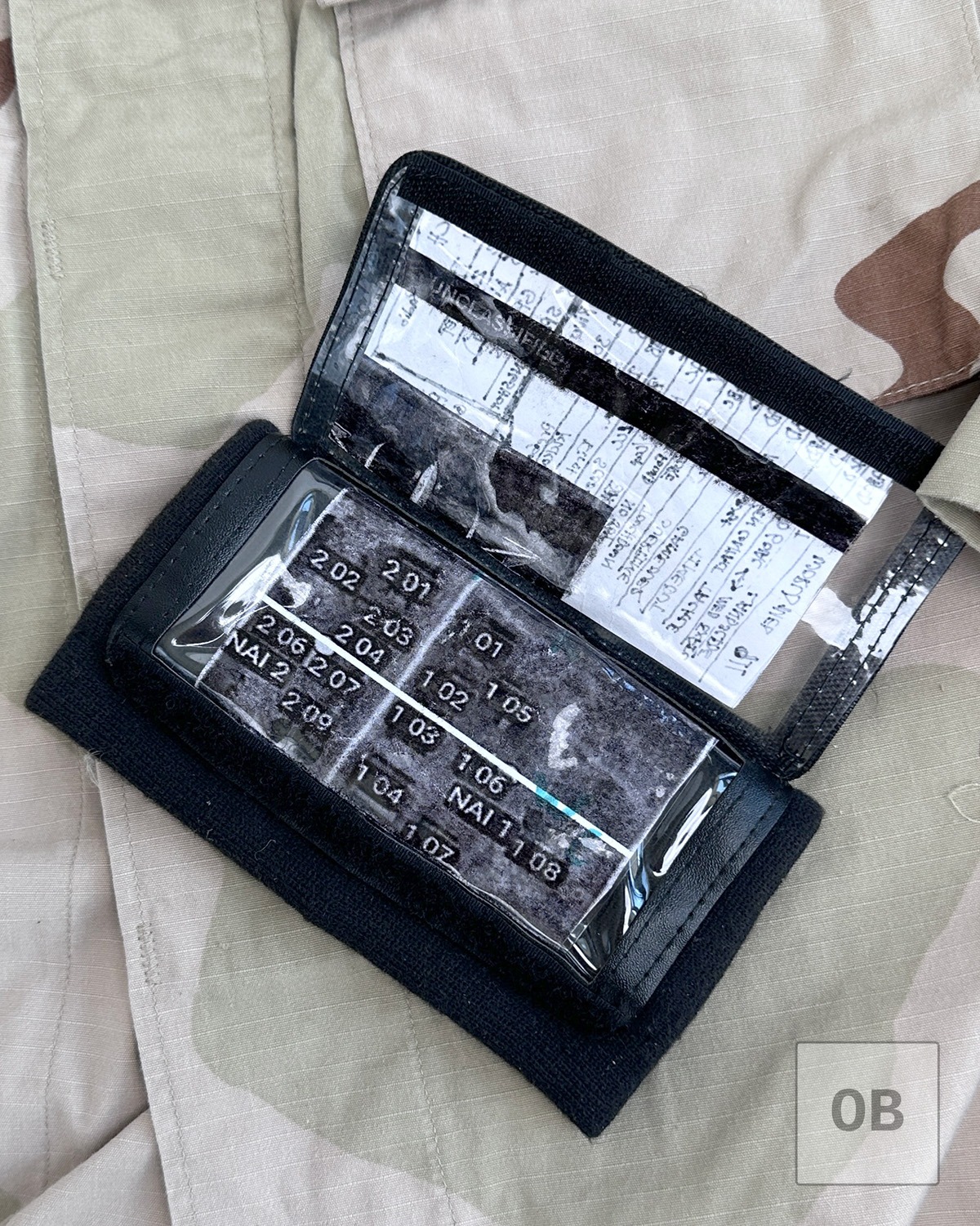 Wrist coach open, showing the target reference grid card and a reused sheet of paper bearing a partial "UNCLASSIFIED" banner.