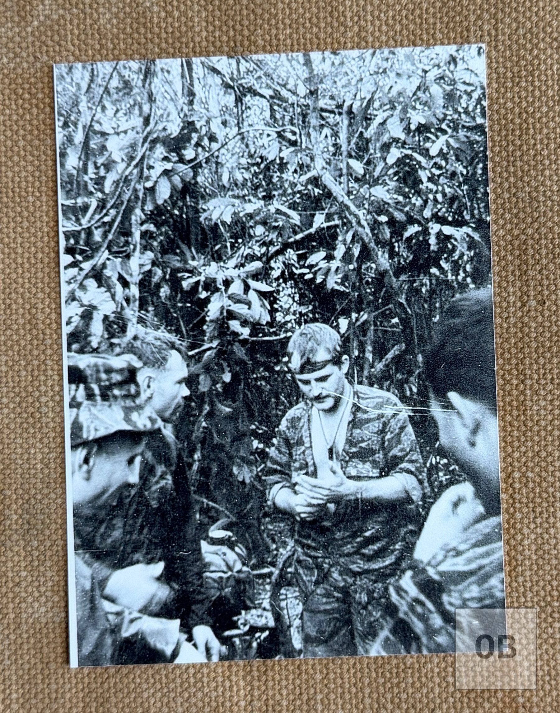 Ulricson in tigerstripe camouflage with a headband, standing in dense jungle, with another soldier in profile at left.