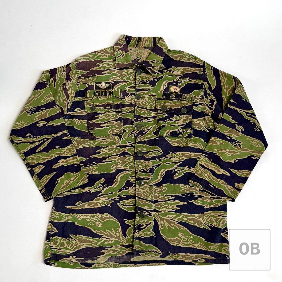 Front of a tigerstripe camouflage shirt with a ULRICSON name tape and a MIKE FORCE tape above the chest pockets, each topped by parachutist wings.