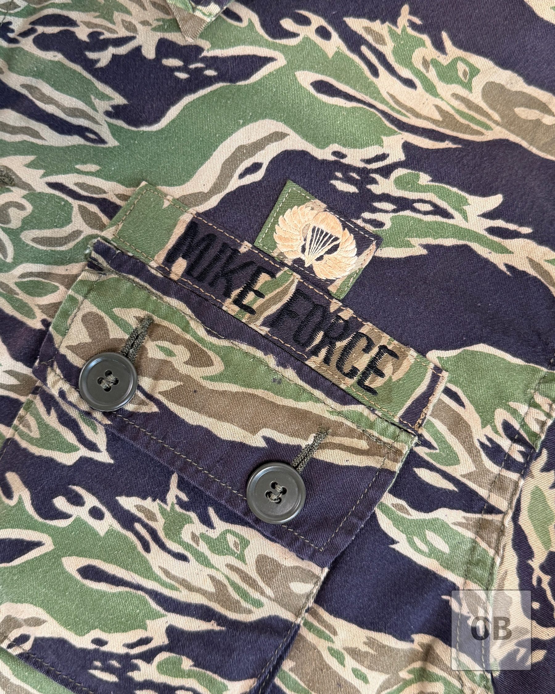 Close-up of the machine-sewn MIKE FORCE tape in lightweight tigerstripe material, with hand-embroidered U.S. jump wings on lightweight tigerstripe above it.