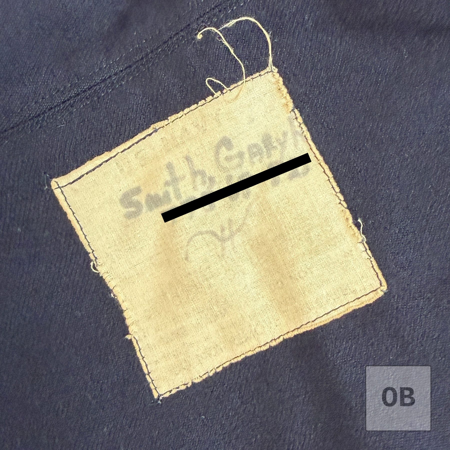 Handwritten name tag sewn inside a SEAL Team 1 dress blue jumper, with the identifying number covered.