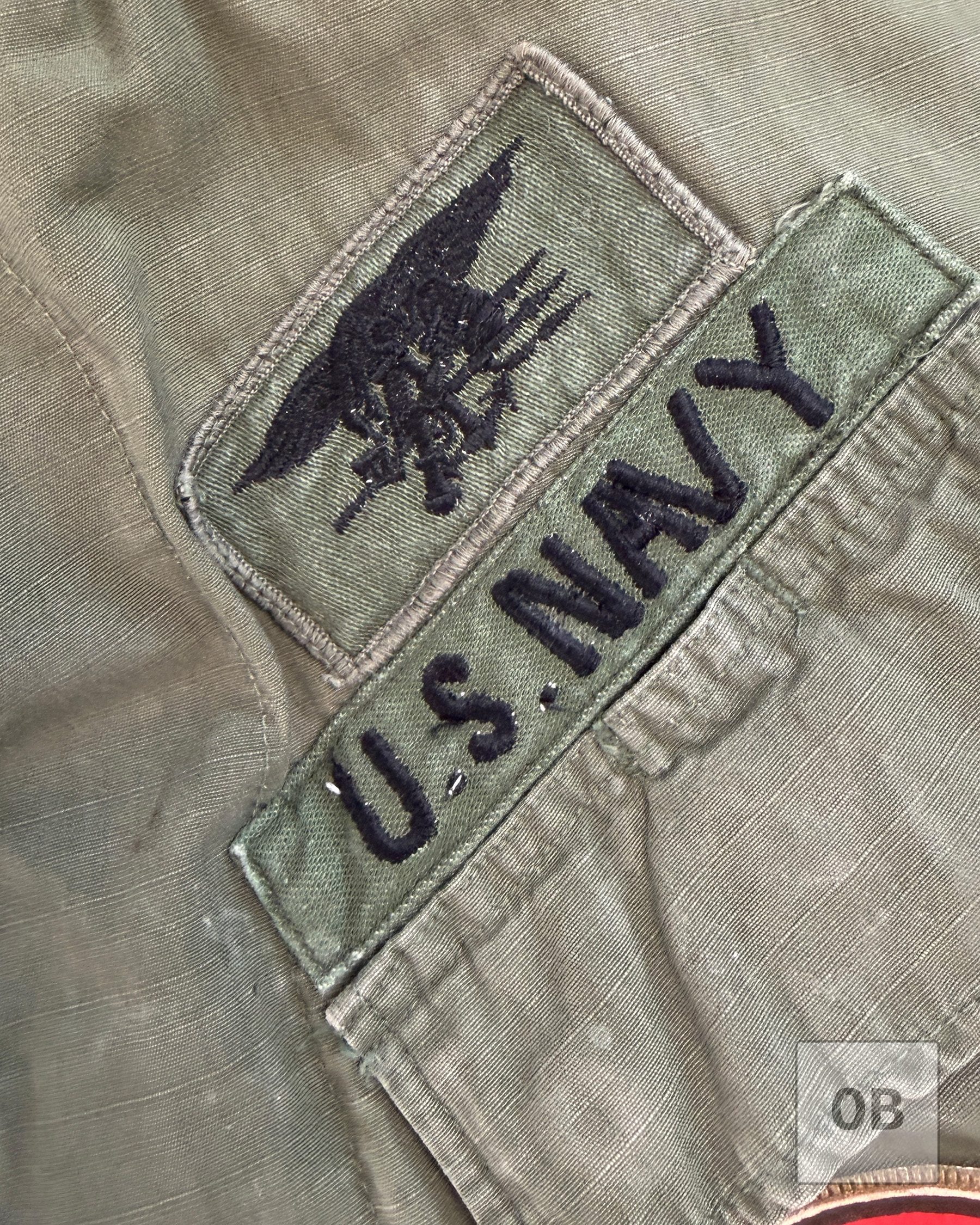 Vietnam-era Navy SEAL Trident embroidered on sateen cloth above a theater-made U.S. NAVY tape on a SEAL Team 1 OD jungle jacket.